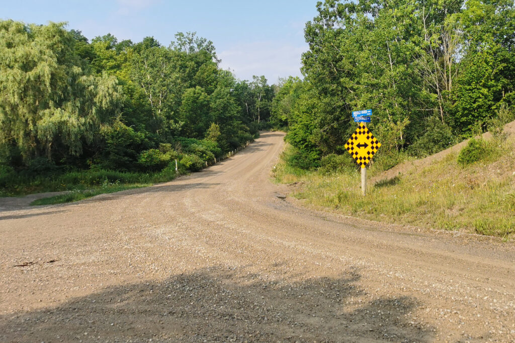A gravel road surrounded by greenery with a sign indicating a fork in the road.
