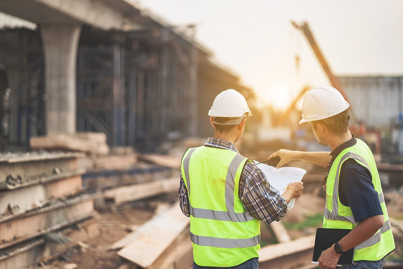 Two construction workers review plans at a bridge construction site.